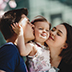 Happy young parents with a little daughter stand under blooming